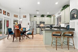 A modern kitchen with stainless steel appliances, a dining area with wooden chairs, and a bar with stools. - Chic 6BR, Pool, Themed Rooms, Near Disney (Kissimmee)