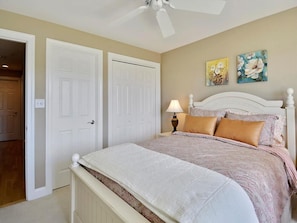 A bedroom with a bed, two doors, a ceiling fan, and two wall-mounted paintings. - Beachside 4BR Condo w/ Ocean Views + Pool Access! (Fenwick Island)