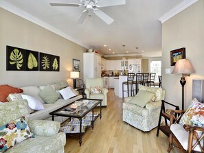 A living room with a sofa, armchairs, and a coffee table. There is a kitchen in the background with cabinets and a dining area. - Beachside 4BR Condo w/ Ocean Views + Pool Access! (Fenwick Island)