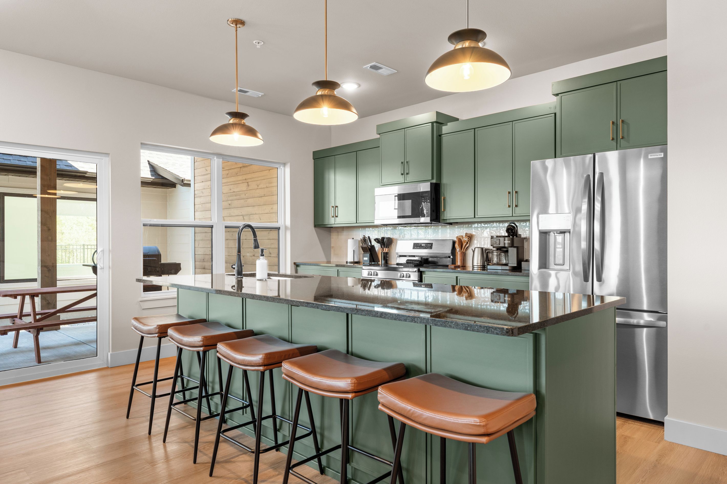 Una cocina moderna con gabinetes verdes, electrodomésticos de acero inoxidable y una barra con taburetes.