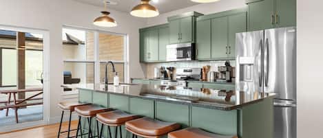 Una cocina moderna con gabinetes verdes, electrodomésticos de acero inoxidable y una barra con taburetes.
