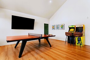 A room with a ping pong table, a flat-screen TV, and a Pac-Man arcade machine. - Putting & Pickle | Private Pool • Games • Lake (Branson)