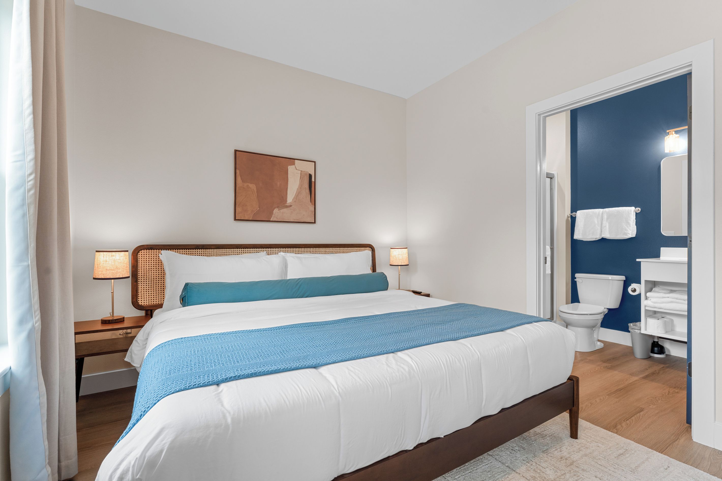 Une chambre d’hôtel bien aménagée, avec un lit, des lampes de chevet, une œuvre d’art accrochée au mur et une vue sur la salle de bain.
