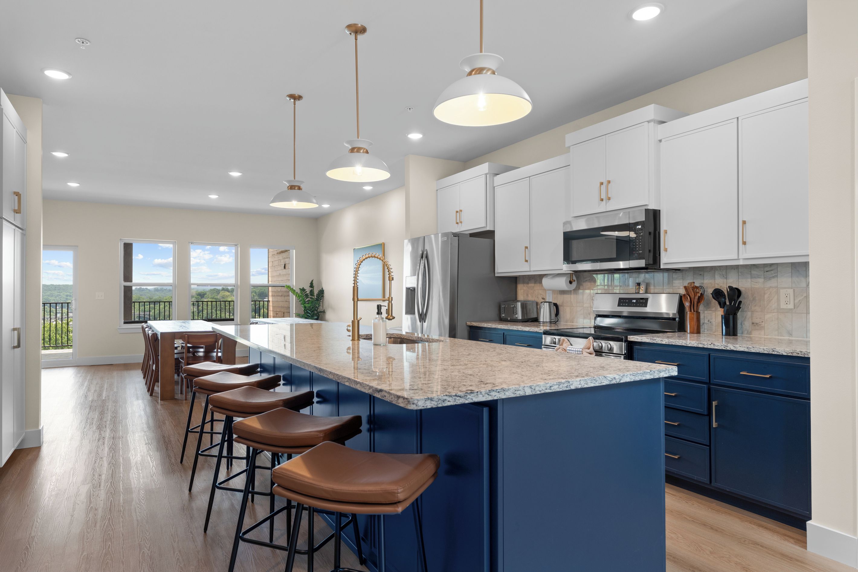 A modern kitchen with a central island, bar stools, and a view to the outside.