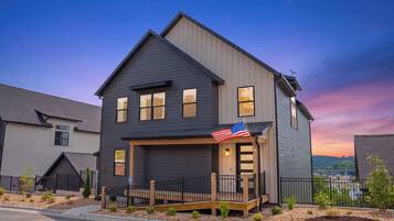 A two-story house with a dark siding exterior, a front porch with a railing, and an American flag.