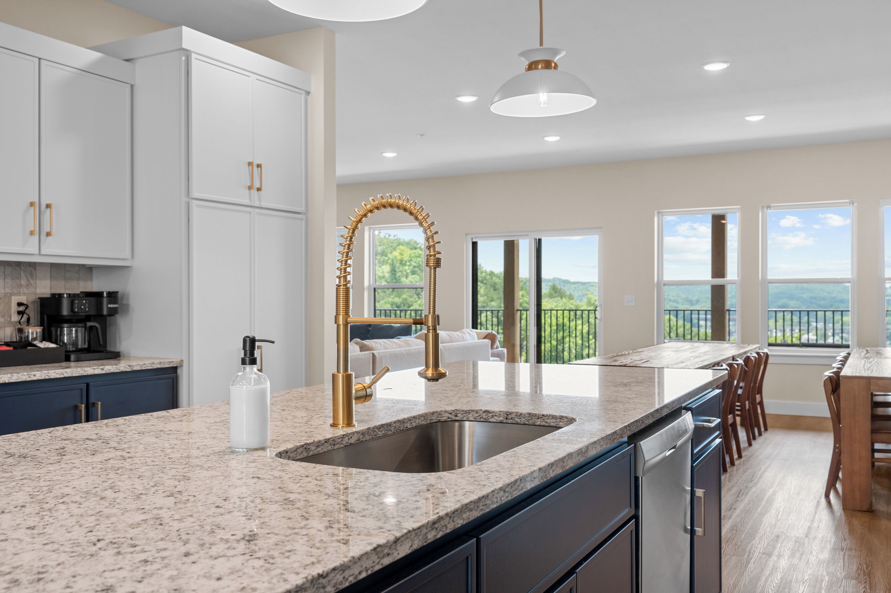 A modern kitchen with a granite countertop, stainless steel sink, and gold faucet.