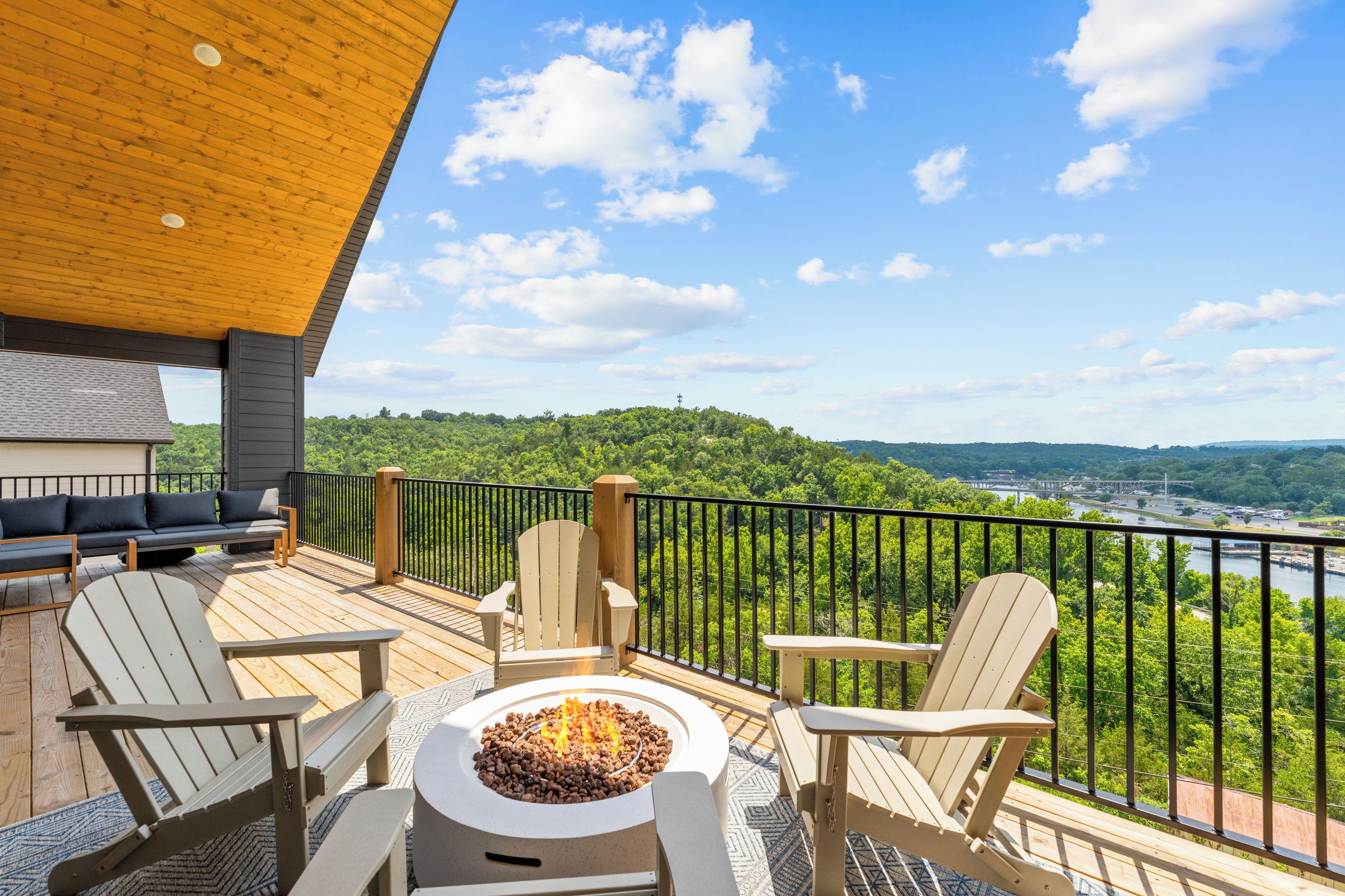 A deck with outdoor furniture, a fire pit, and a scenic view of a river and forest.