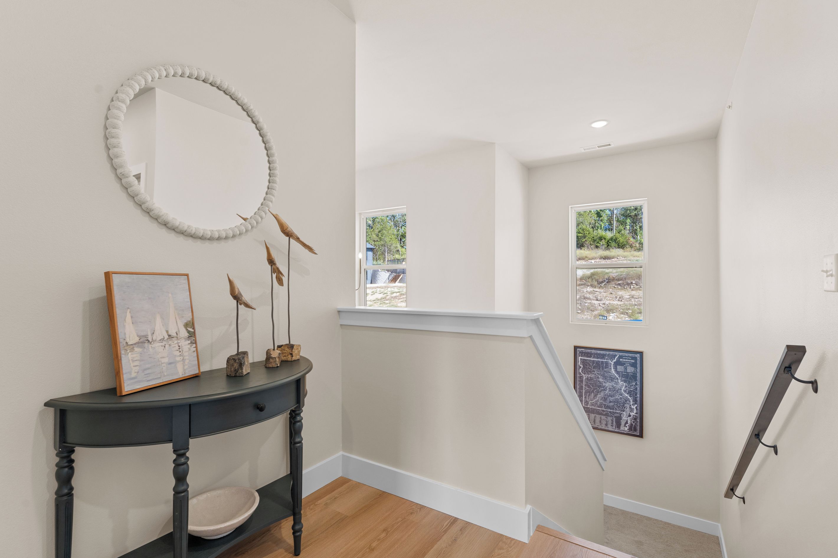 A staircase with a view of the outdoors, a wall-mounted mirror, a console table with a framed picture, and a map.