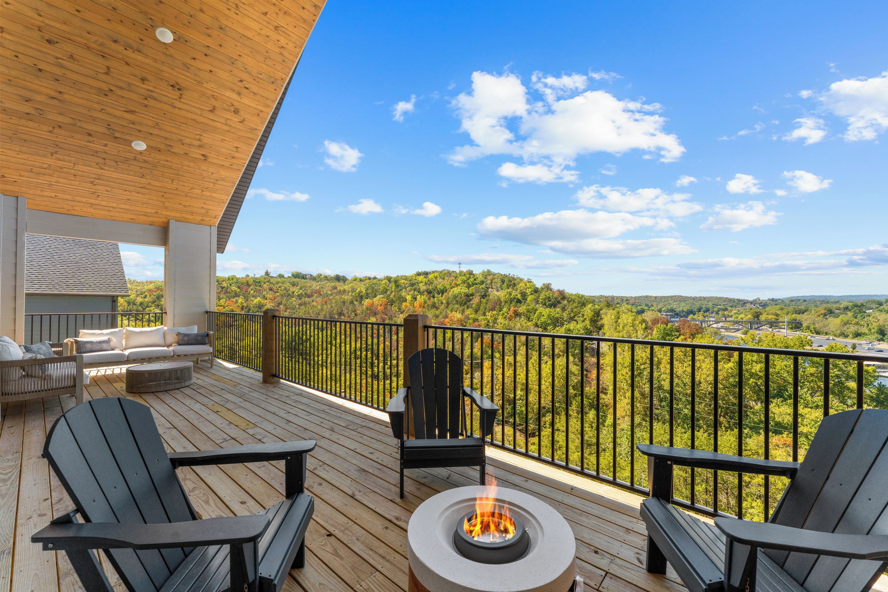 Eine Holzterrasse mit Sitzgelegenheit im Freien, einer Feuerstelle und Blick auf eine bewaldete Landschaft.