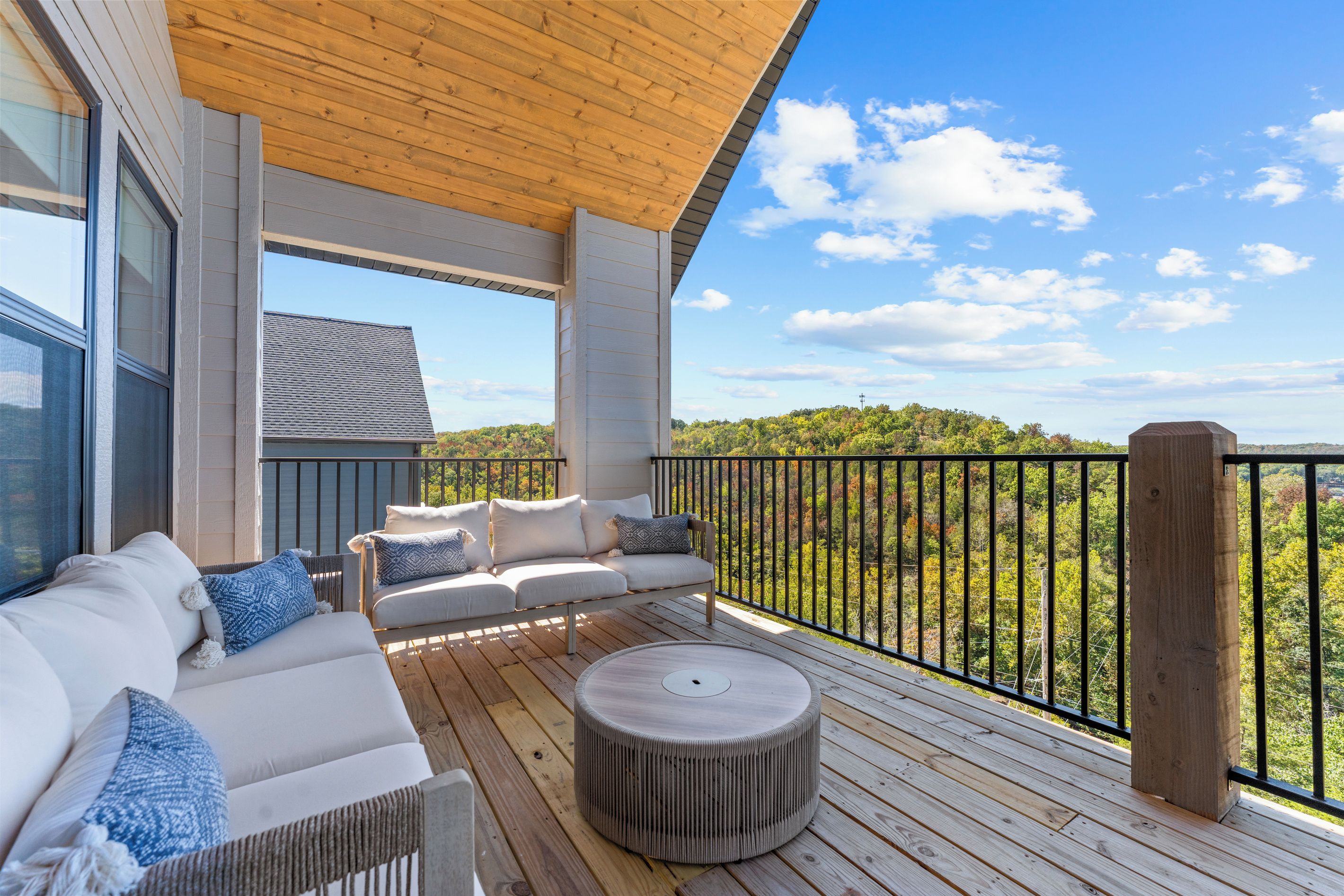 Un espacio de estar al aire libre techado, con terraza de madera, un conjunto de sofás y una mesa redonda.