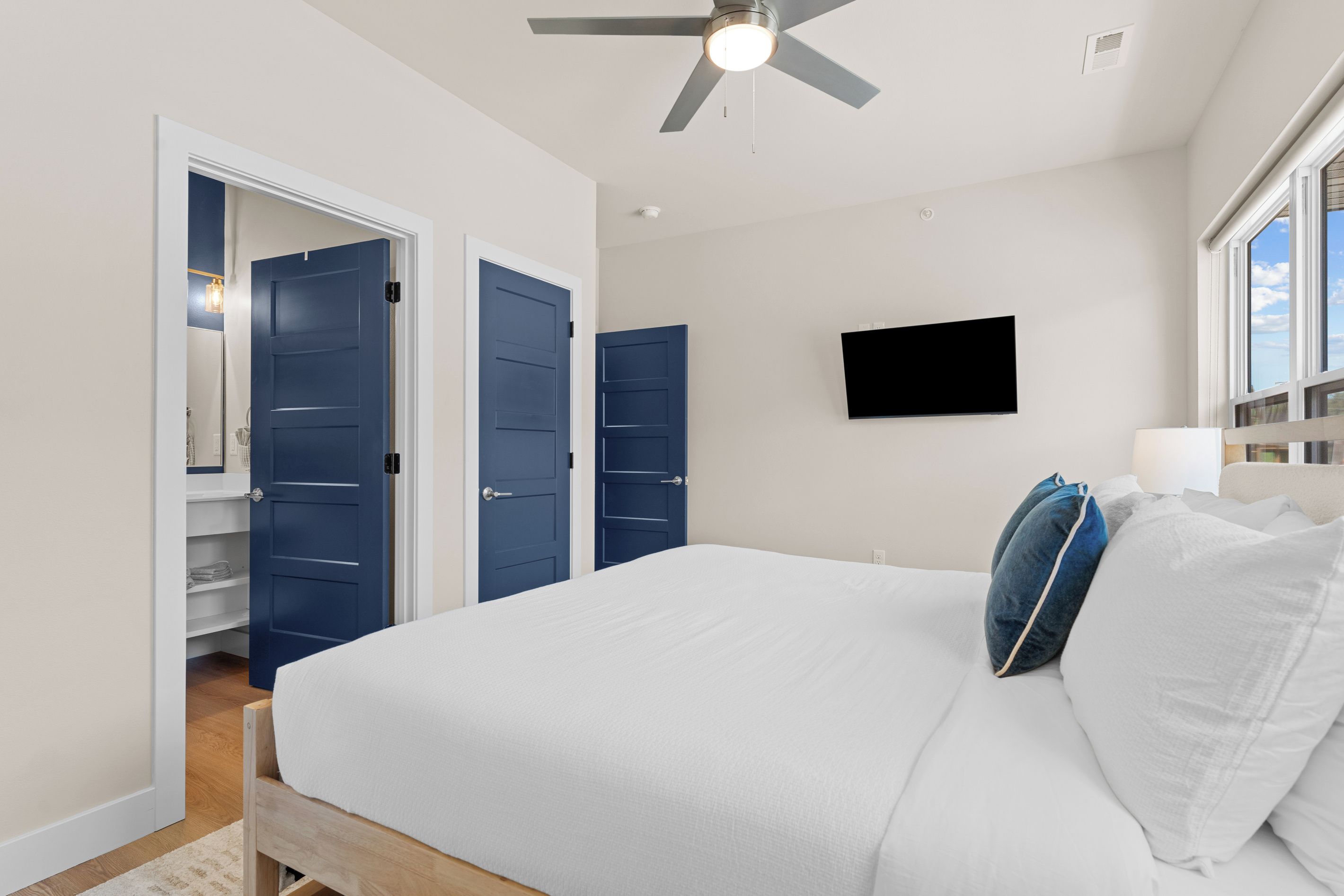 A bedroom with a bed, a ceiling fan, a TV, and a window.
