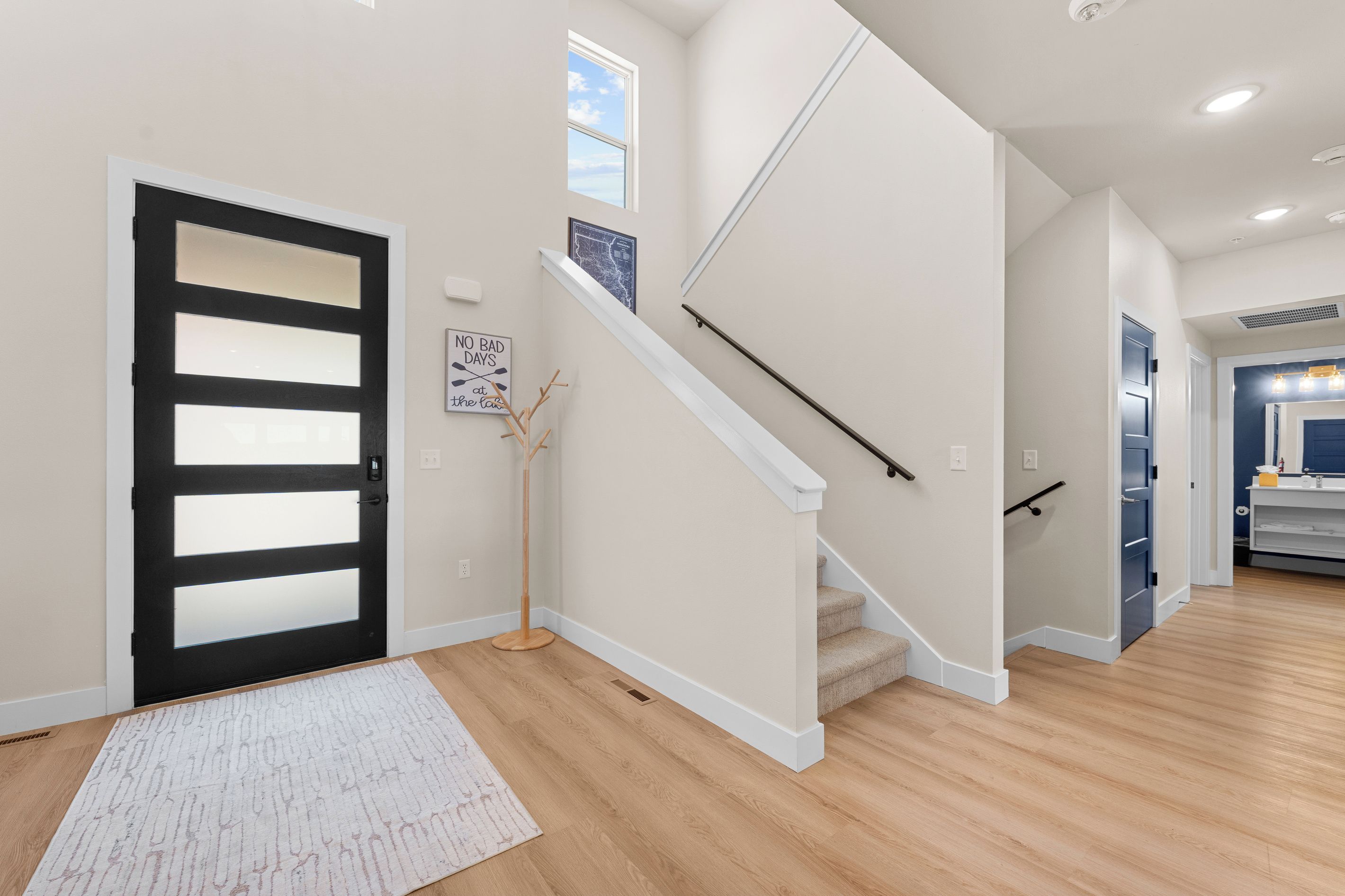 Ein modernes Interieur mit einer Treppe, einer Tür mit schwarzem Rahmen, einem weißen Teppich und einem an der Wand befestigten Schild.