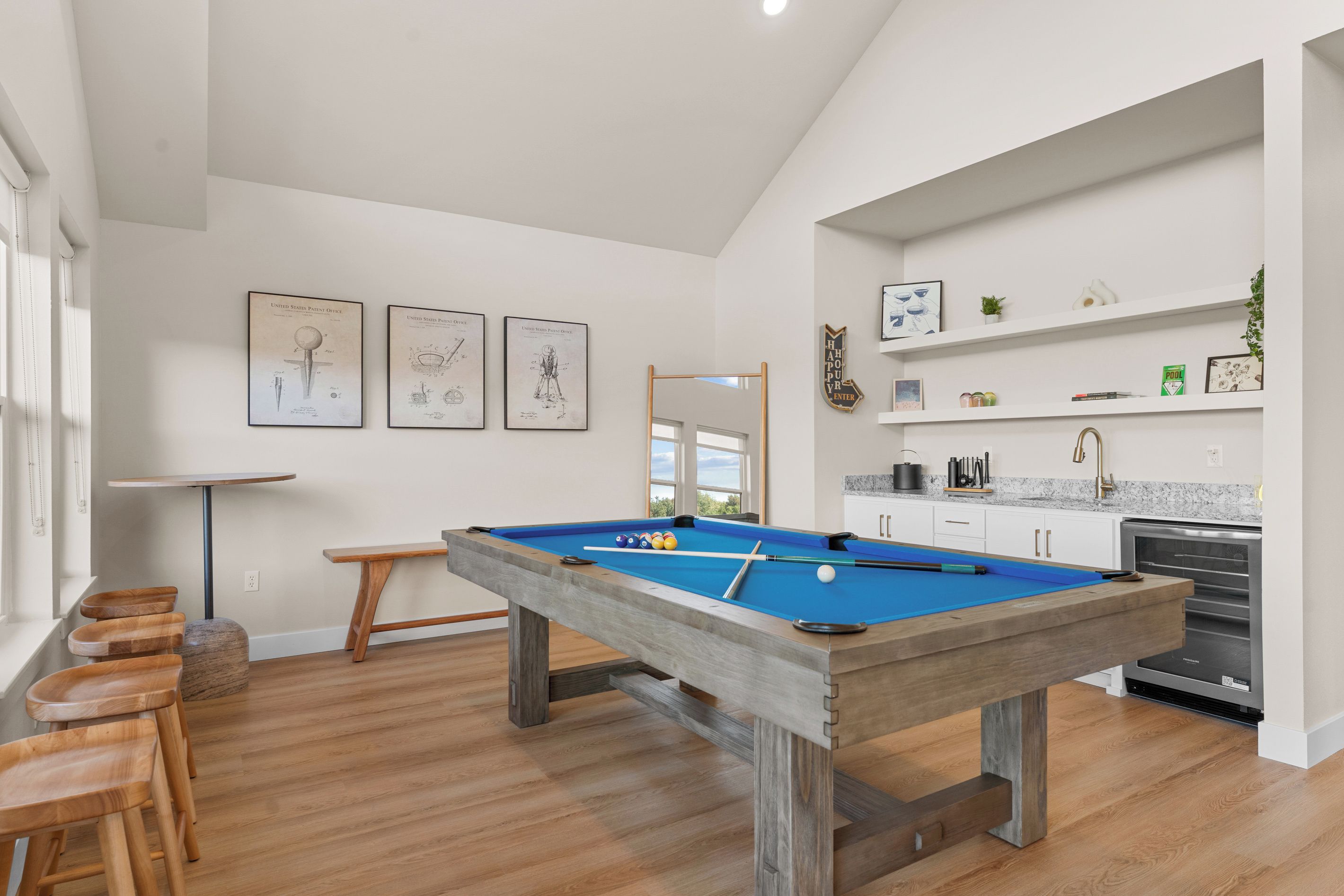 A modern kitchen with a built-in pool table, wooden stools, and a dining table.