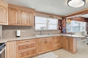 A kitchen with wooden cabinets, a sink, and a window with blinds. - Sea Turtle Nest | Oceanfront Cottage | Private Beach Access | Dog Friendly | Flagler Beach (Flagler Beach)