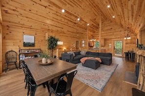 A wooden cabin interior with a dining area, sofa, and kitchen. - Mountain Views | Hot Tub • Firepit • Game Room (Sevierville)