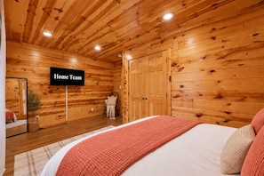 A wooden-paneled room with a bed, a chair, a plant, and a sign that reads 'Home Team'. - Mountain Views | Hot Tub • Firepit • Game Room (Sevierville)