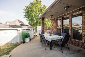 Eine Außenpatio mit Tisch und Stühlen, eine Ziegelwand und ein Baum im Hintergrund.