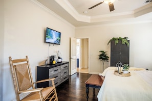 Ein Hotelzimmer mit Holzstuhl, Schreibtisch mit Kaffeemaschine, Wandfernseher, Bett mit weißer Bettdecke und dunklem Holzschrank.