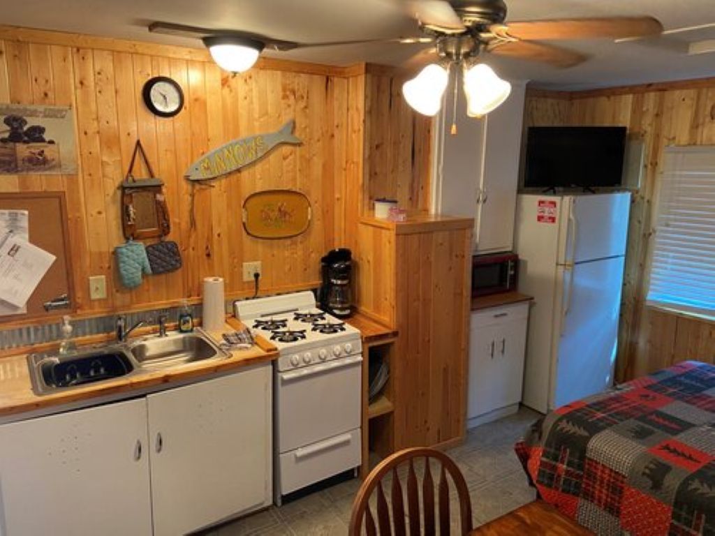 Une cuisine de taille réduite avec des murs en bois, une cuisinière, un évier et un réfrigérateur.