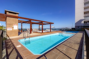 Ein Pool auf dem Dach mit einer Holzpergola, Liegestühlen und Blick aufs Meer.