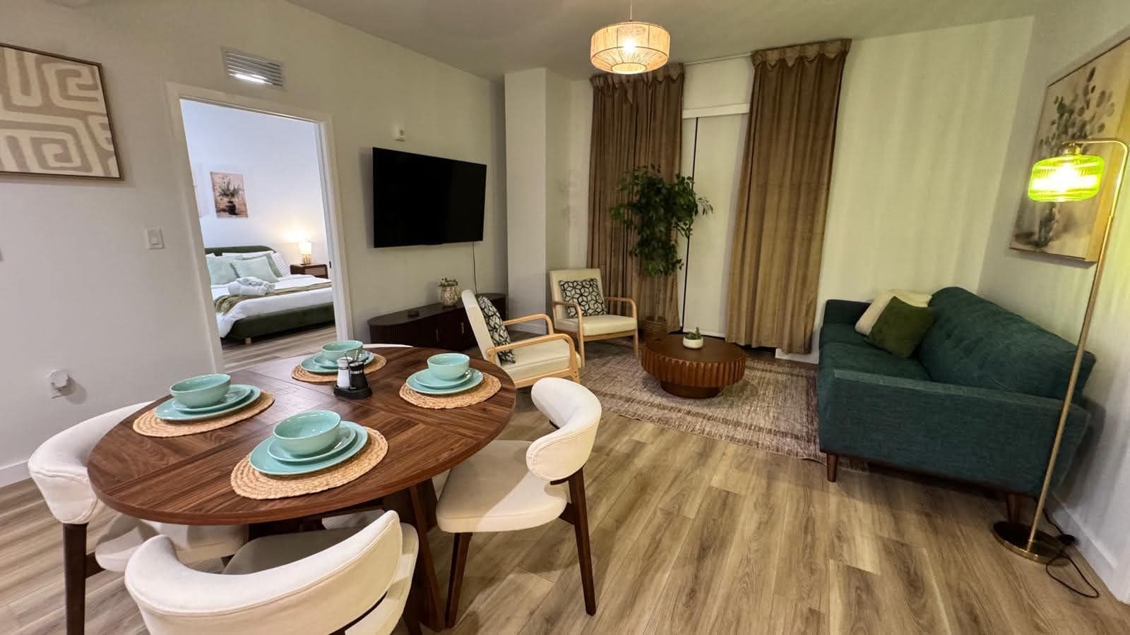 A modern living room with a dining table set for four, a sofa, a television, and a floor lamp.