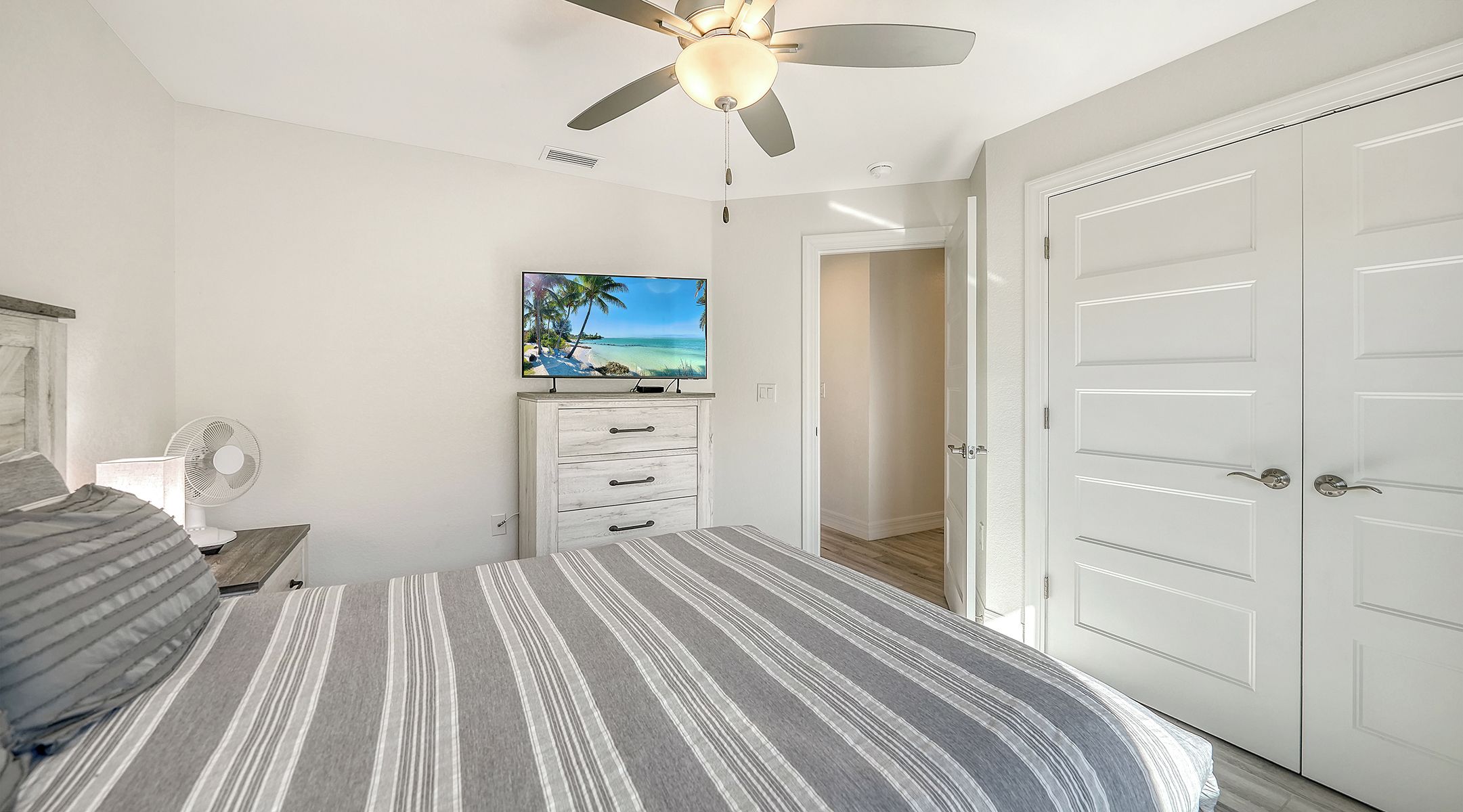 A bedroom with a bed, a ceiling fan, a TV, and a wardrobe.