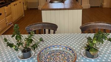 Un coin repas avec une table dressée pour deux personnes, agrémentée d’une nappe à pois bleus, de deux plantes en pot et d’une assiette décorative.