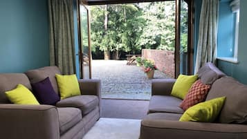 A room with two sofas and a small table, a window with curtains, and a view of a garden.