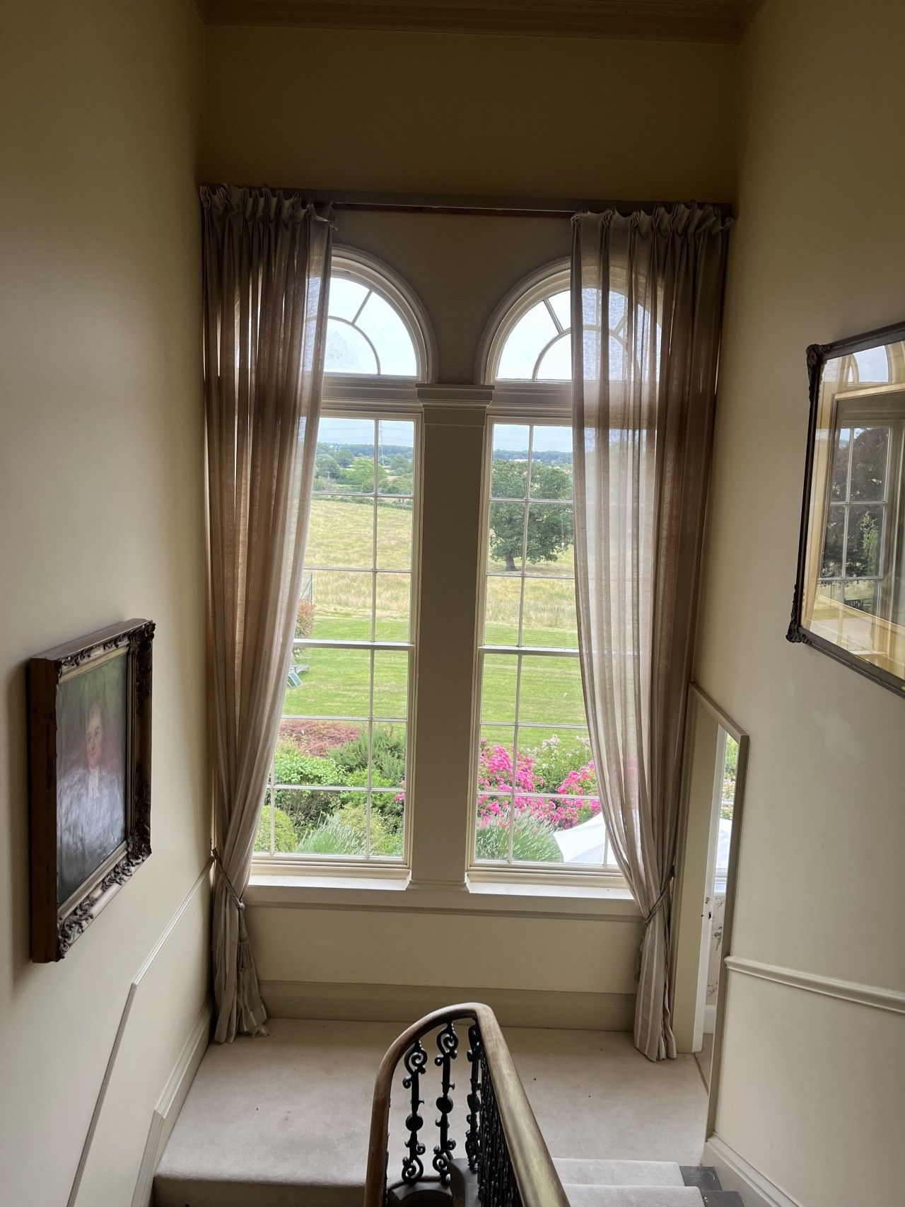Een kamer met uitzicht op een tuin door een raam met gordijnen.