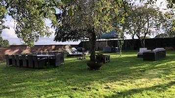 Et udendørs opholdsområde med et bord, stole, en bålplads og liggestole.