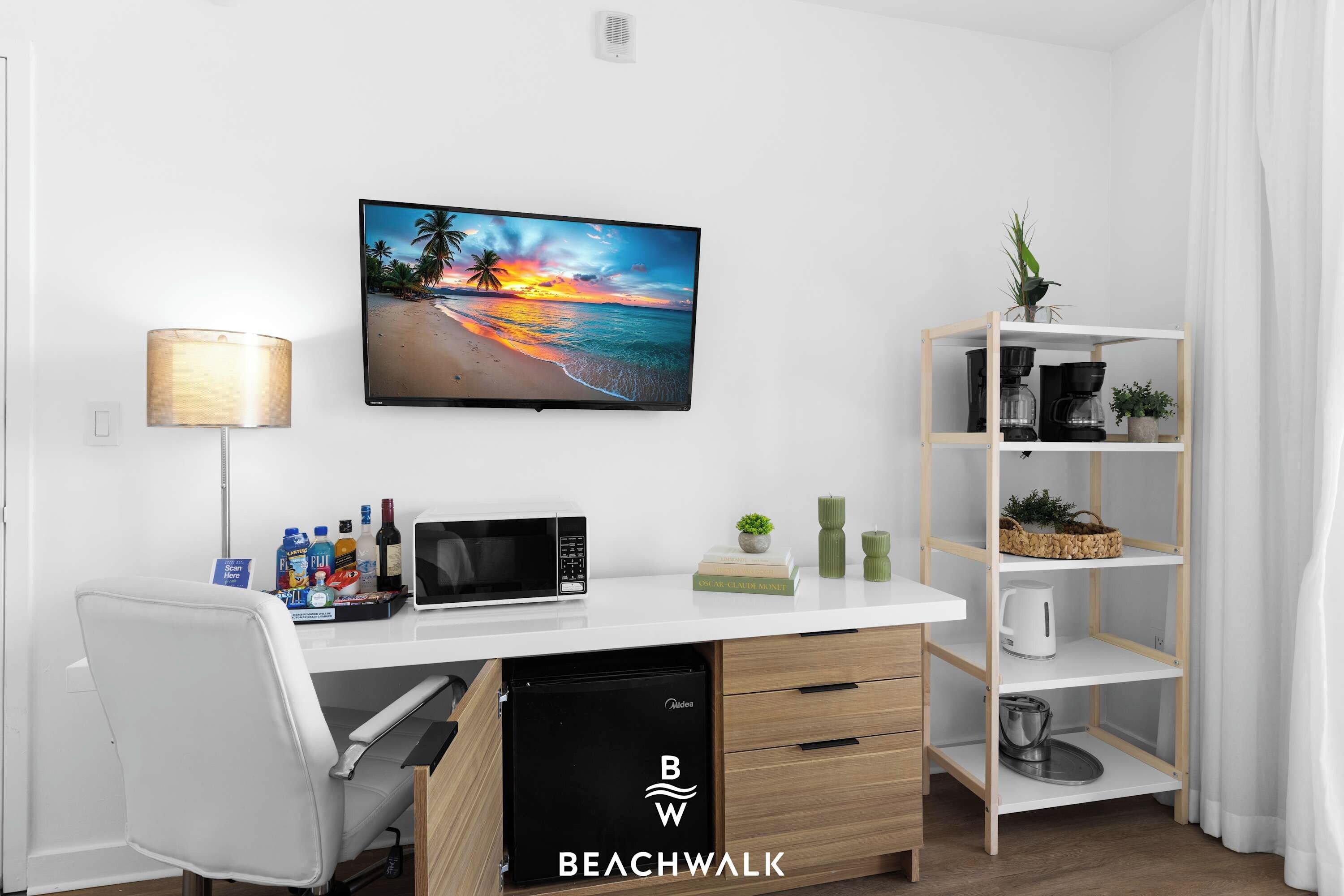 Una habitación moderna con un escritorio blanco, un televisor de pantalla plana, un microondas, una estantería y una pequeña planta.