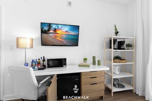 Habitació moderna amb escriptori blanc, televisió de pantalla plana, microones, prestatgeria i una petita planta.