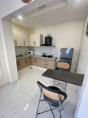 Cocina compacta equipada con microondas, estufa y refrigerador. Cuenta con una mesa de comedor y sillas.