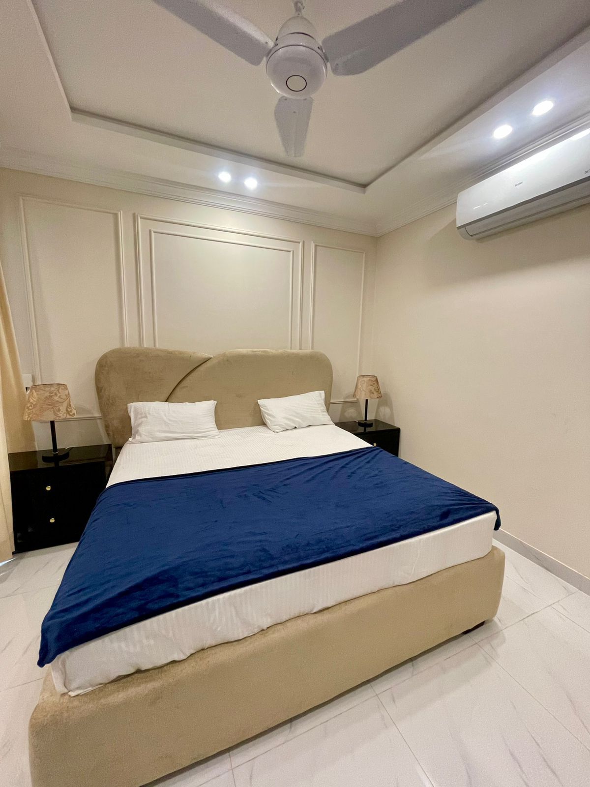 Un dormitorio con una cama, mesitas de noche, ventilador de techo y aire acondicionado.
