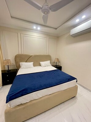 Un dormitorio con una cama, mesitas de noche, ventilador de techo y aire acondicionado.