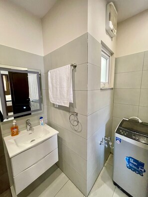 Un baño con lavamanos, espejo, perchero para toallas y ducha eléctrica portátil.
