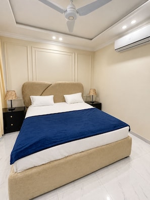 Un dormitorio con cama, mesitas de noche, ventilador de techo y aire acondicionado.