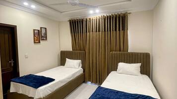 Ein Hotelzimmer mit zwei Einzelbetten, einem Deckenventilator und einem fensterbepflanzten Fenster.