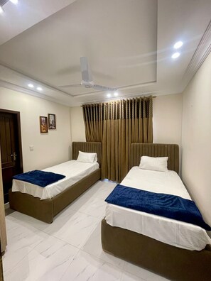 Una habitación de hotel con dos camas individuales, un ventilador de techo y una ventana con cortinas.