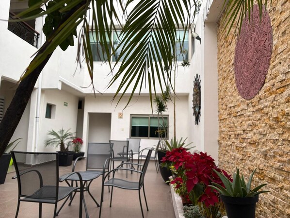 An outdoor seating area with chairs and tables, surrounded by potted plants and a decorative wall.