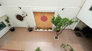 A spacious indoor area with a tiled floor, a decorative wall with a circular pattern, and various potted plants.
