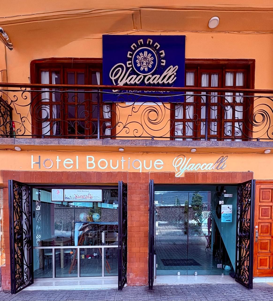 Een boetiekhotel met een bord waarop staat 'Hotel Boutique Yao cali' en een balkon met decoratieve leuningen.