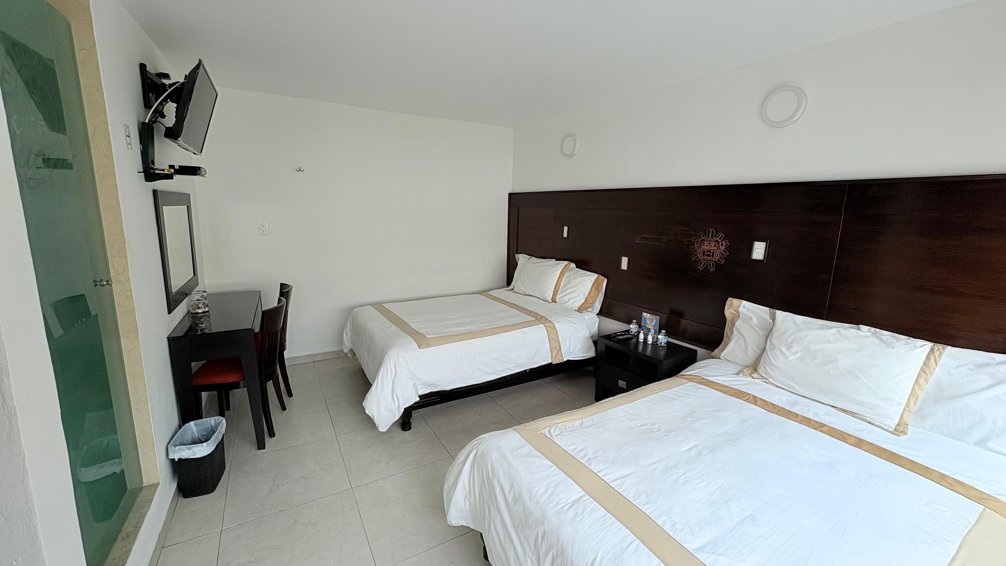 A hotel room with two beds, a desk, a chair, and a television mounted on the wall.
