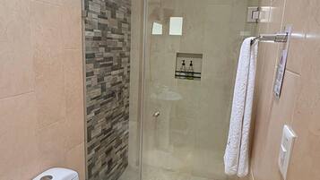 A modern bathroom with a glass-enclosed shower, a white toilet, and a stone-patterned wall.