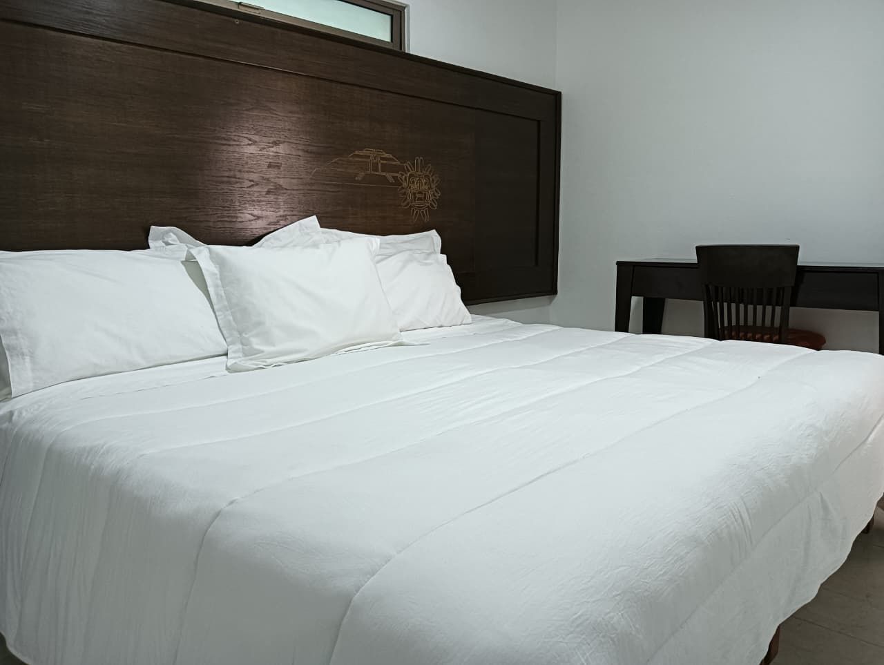 Un lit bien fait, avec du linge de lit blanc, dans une chambre d’hôtel.