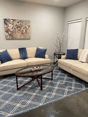 Ein Wohnzimmer mit zwei Sofas, einem Couchtisch, einem Teppich und einem Bild an der Wand.