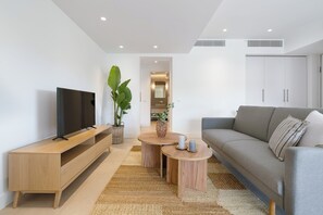 Ein modernes Wohnzimmer mit Flachbildfernseher, einem grauen Sofa, einem Holztisch und einer großen Pflanze.