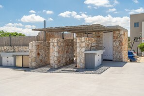 An outdoor patio area with stone walls, a wooden fence, and a covered seating area. - Le Mont Blanc | 2-Bedroom Apartment with Shared Pool (Kounoupidiana)