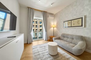 Ein modernes Wohnzimmer mit einer Couch, einem Couchtisch, einem Flachbildfernseher und einer Schiebetür zu einem Außenbalkon.