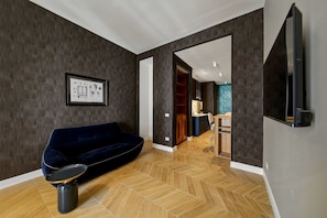 A modern living room with a dark blue sofa, a coffee table, and a herringbone wooden floor. There is a framed picture on the wall and a television mounted on the wall. - Apartment 'Luxury Toledo Blu' with Balcony, Wi-Fi and Air Conditioning (Napoli)
